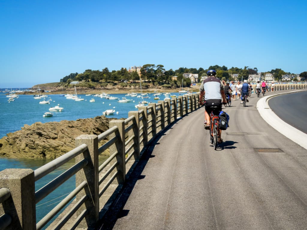 Ciclisti su una passerella panoramica lungo la costa della Bretagna, Francia, con vista sul mare, da Arromanches a St. Malo